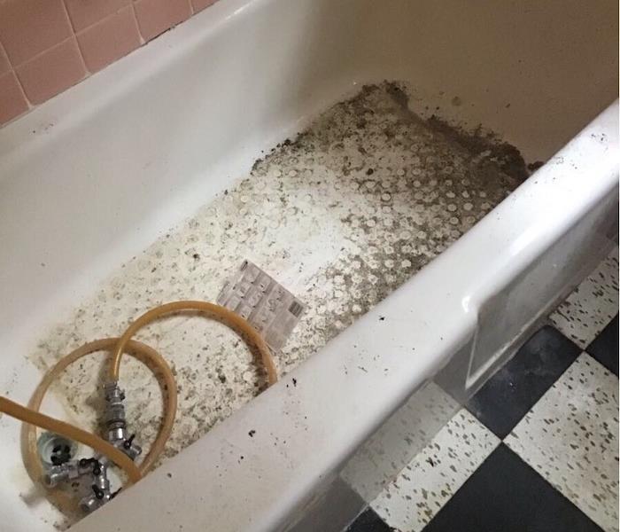 Bathtub with dirt and debris and dirty black and white floor