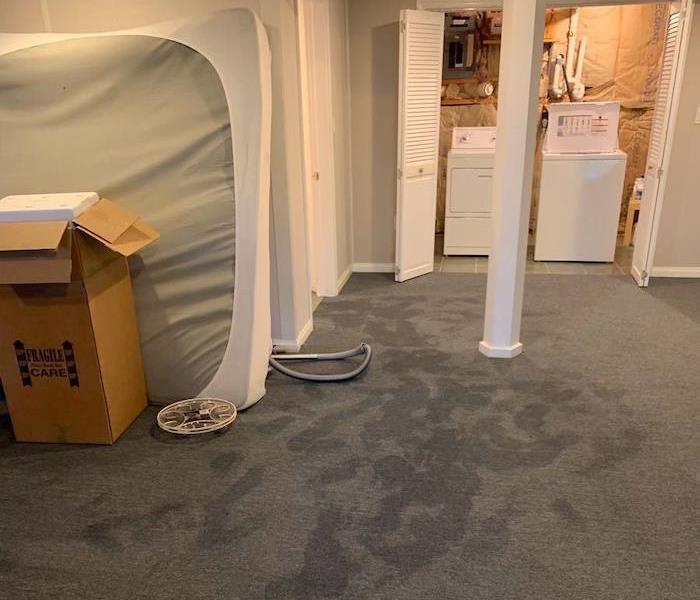 Basement with wet carpet and mattress up against a wall
