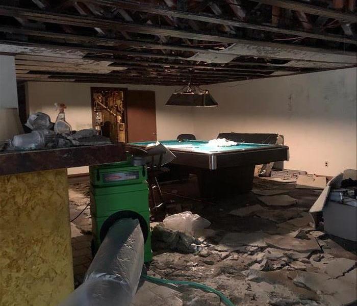 : Basement game room with severe water damage with debris on the floor and air scrubber